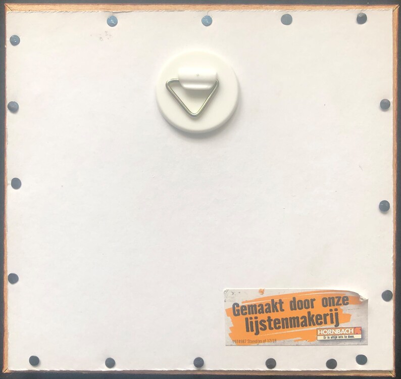 Puede incluir: Parte trasera de un cuadro enmarcado con un fondo blanco, un colgador de metal y una etiqueta con texto en holand&eacute;s. El marco es negro con borde de madera y peque&ntilde;as tachuelas negras.