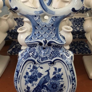 May include: A blue and white ceramic candelabra with a peacock design. The candelabra has three arms and a base with a floral pattern.