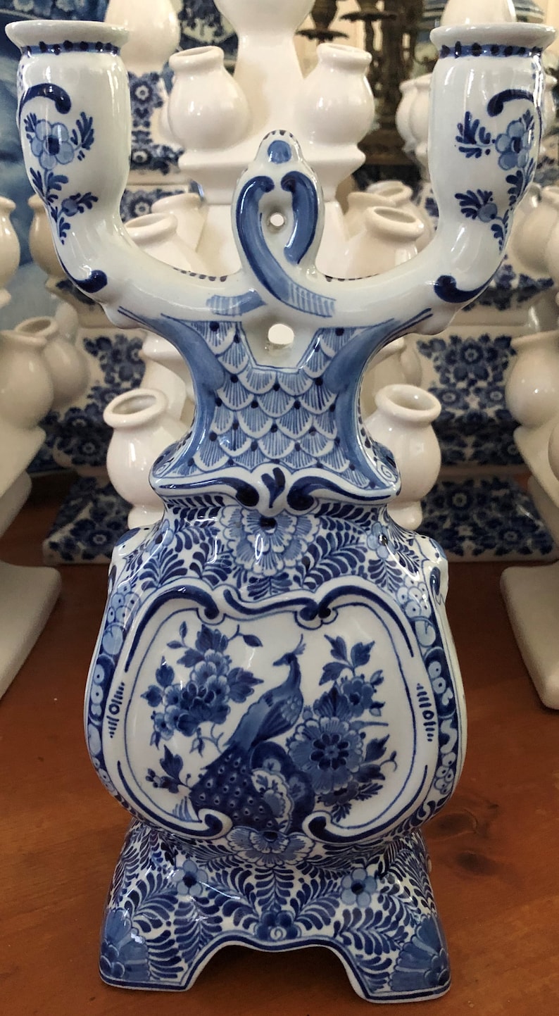 May include: A blue and white ceramic candelabra with a peacock design. The candelabra has three arms and a base with a floral pattern.