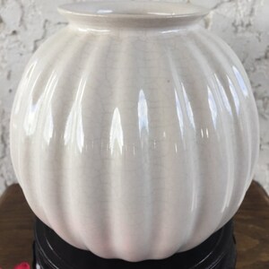 May include: White ceramic vase with a ribbed design and a crackled glaze. The vase is sitting on a black wooden stand.