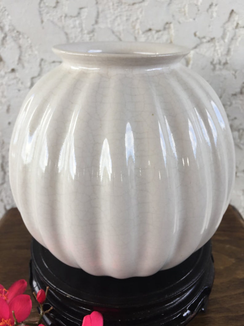 May include: White ceramic vase with a ribbed design and a crackled glaze. The vase is sitting on a black wooden stand.