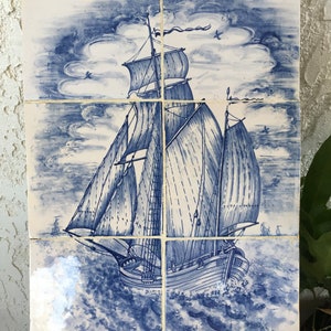 Puede incluir: Un azulejo de cer&aacute;mica azul y blanco que representa un barco de vela con velas hinchadas contra un cielo nublado. El barco navega en un mar agitado con olas. El azulejo est&aacute; firmado "MARKWITZ" en la esquina inferior derecha.