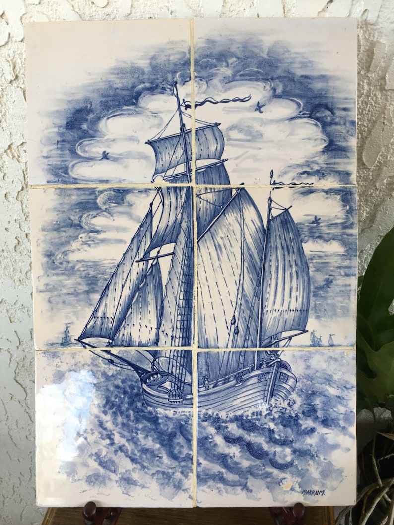 Puede incluir: Un azulejo de cer&aacute;mica azul y blanco que representa un barco de vela con velas hinchadas contra un cielo nublado. El barco navega en un mar agitado con olas. El azulejo est&aacute; firmado "MARKWITZ" en la esquina inferior derecha.