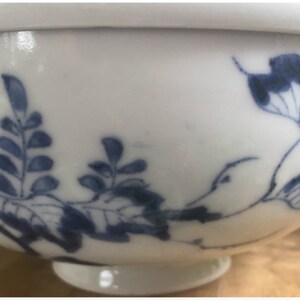 May include: White porcelain bowl with blue floral and leaf patterns. The bowl has a small, attached dish in the center. The design is repeated on the underside of the bowl. The bowl is a traditional Asian design.