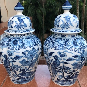 May include: Two matching blue and white ceramic jars with lids. The jars feature intricate floral and bird designs. The lids are topped with a blue finial. The jars are a classic decorative item.