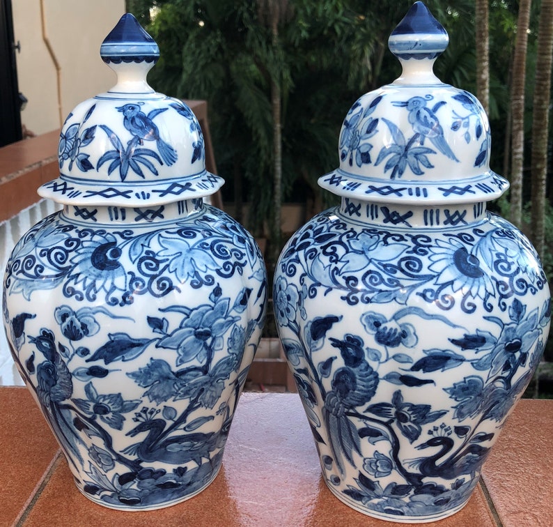 May include: Two matching blue and white ceramic jars with lids. The jars feature intricate floral and bird designs. The lids are topped with a blue finial. The jars are a classic decorative item.