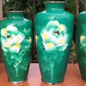 Puede incluir: Cuatro jarrones japoneses de cloisonn&eacute; verde y blanco con dise&ntilde;os florales. Los jarrones son de diferentes tama&ntilde;os y est&aacute;n dispuestos en una fila del m&aacute;s grande al m&aacute;s peque&ntilde;o.