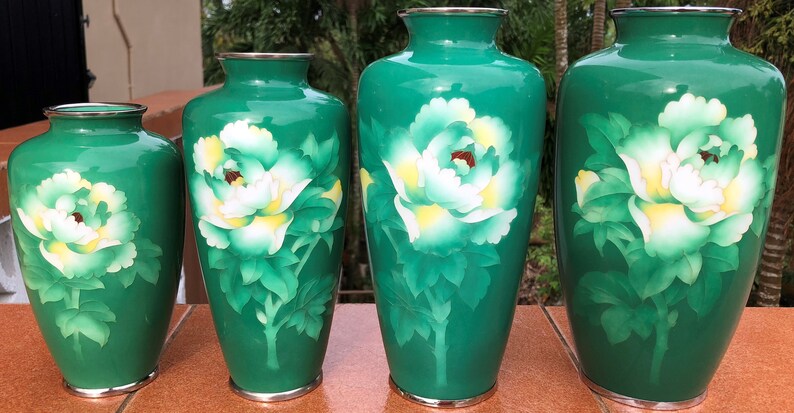 Puede incluir: Cuatro jarrones japoneses de cloisonn&eacute; verde y blanco con dise&ntilde;os florales. Los jarrones son de diferentes tama&ntilde;os y est&aacute;n dispuestos en una fila del m&aacute;s grande al m&aacute;s peque&ntilde;o.