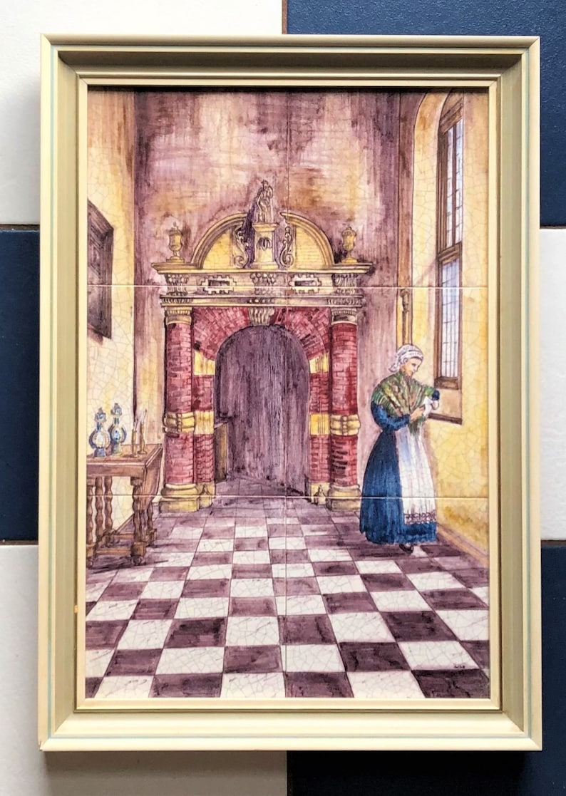 Puede incluir: Un azulejo de cer&aacute;mica enmarcado que representa a una mujer con un vestido azul y un delantal blanco de pie en una habitaci&oacute;n enlosada con un suelo de ajedrez. La habitaci&oacute;n tiene una gran puerta arqueada con un marco de ladrillo rojo y dorado. El azulejo est&aacute; enmarcado en un marco de madera claro.