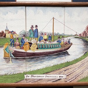 May include: A vintage tile painting depicting a canal scene with a boat full of people. The boat is being pulled by a rope attached to a horse on the towpath. The tile is titled "De Trekschuit Omstreeks 1850".