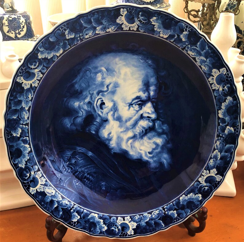 Pu&ograve; includere: Un piatto in ceramica blu e bianco con un ritratto dettagliato di un uomo con la barba. Il piatto ha un bordo ondulato ed &egrave; decorato con motivi floreali.
