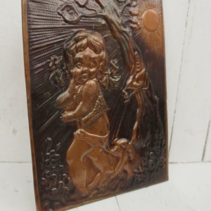 May include: A copper wall plaque with a raised relief design of a child holding a flower and standing next to a tree. The plaque has a sun and a floral design in the background.