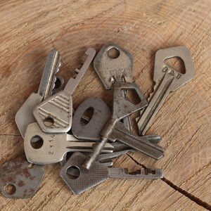 May include: A collection of vintage keys with various designs and finishes, including a rusty key, a key with a number "21114" on it, and a key with the text "9AU" on it. The keys are arranged on a wooden surface.