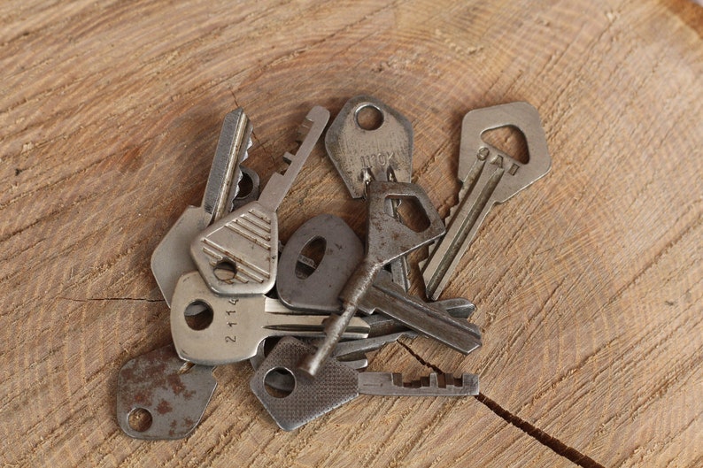 May include: A collection of vintage keys with various designs and finishes, including a rusty key, a key with a number "21114" on it, and a key with the text "9AU" on it. The keys are arranged on a wooden surface.