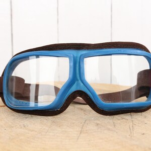 May include: Blue and brown safety goggles with clear lenses. The goggles have a wide, wraparound design and are made of plastic.