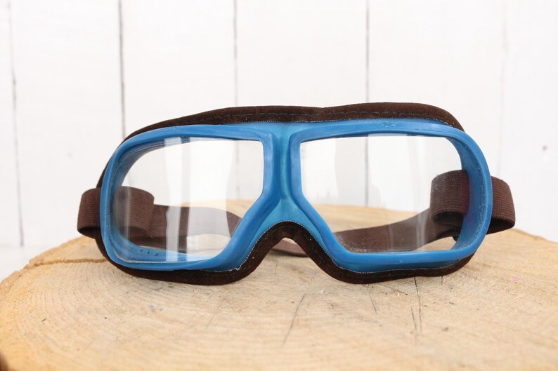 May include: Blue and brown safety goggles with clear lenses. The goggles have a wide, wraparound design and are made of plastic.