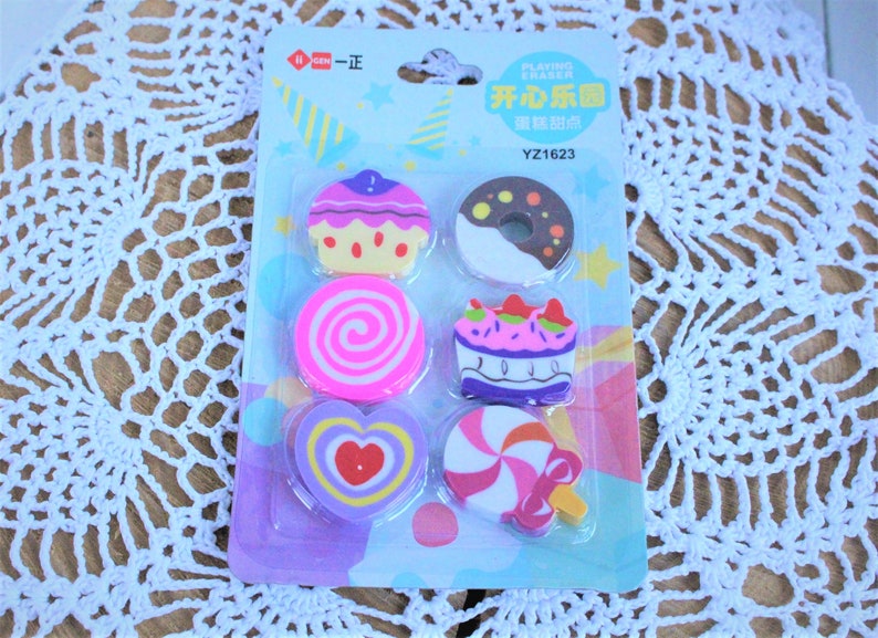 K&ouml;nnte beinhalten: Ein Set mit sechs bunten Radiergummis in Form verschiedener Desserts. Die Radiergummis sind auf einer blauen und wei&szlig;en Karte mit dem Text "Playing Eraser" und "YZ1623" verpackt.