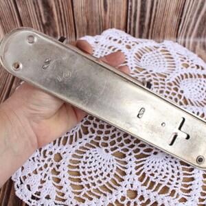 K&ouml;nnte beinhalten: Ein silberner T&uuml;rgriff aus Metall mit rechteckiger Form und einem kreuzf&ouml;rmigen Design. Der Griff hat an jedem Ende zwei L&ouml;cher und den Text "2" und "U.S." auf der Oberfl&auml;che.