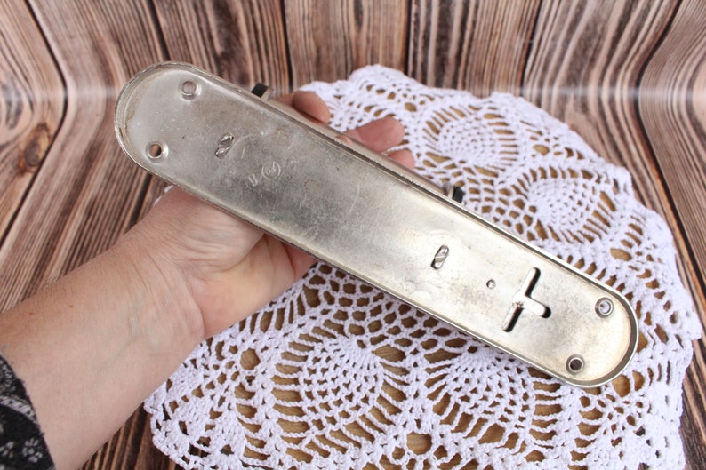 K&ouml;nnte beinhalten: Ein silberner T&uuml;rgriff aus Metall mit rechteckiger Form und einem kreuzf&ouml;rmigen Design. Der Griff hat an jedem Ende zwei L&ouml;cher und den Text "2" und "U.S." auf der Oberfl&auml;che.