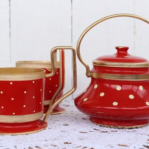 May include: Red and gold polka dot tea set with a teapot and two cups. The teapot has a lid and a handle. The cups have handles and a base.