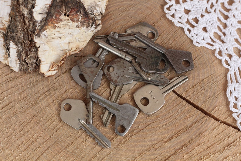May include: A collection of vintage keys with various designs and finishes, including a key with the number "2114" engraved on it. The keys are arranged on a wooden surface.