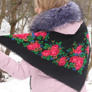 Op de afbeelding: Een zwarte driehoekige sjaal met een bloemenpatroon in tinten rood, roze, groen, blauw en geel. De sjaal heeft een gefranst randje.
