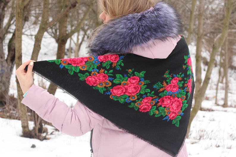 Op de afbeelding: Een zwarte driehoekige sjaal met een bloemenpatroon in tinten rood, roze, groen, blauw en geel. De sjaal heeft een gefranst randje.