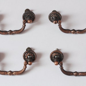 May include: Set of four antique-style cabinet pulls with a copper finish. Each pull has a decorative, ornate design and a round knob.