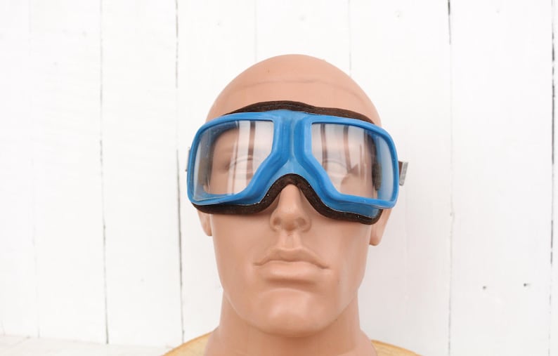 May include: Blue safety goggles with a black strap and clear lenses. The goggles are on a mannequin head.