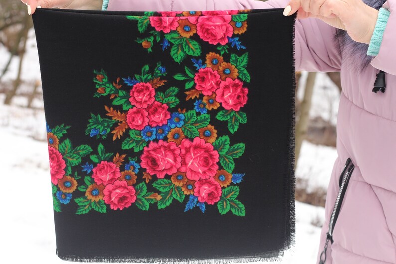 Op de afbeelding: Een zwarte sjaal met een bloemenpatroon in tinten roze, groen, blauw en bruin. De sjaal heeft een gefranst randje.