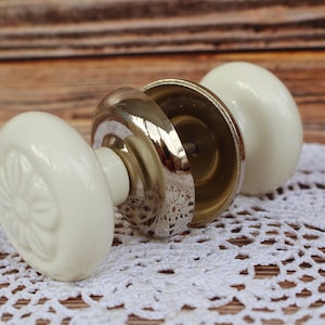May include: White ceramic door knob with a floral design and a silver metal backplate.