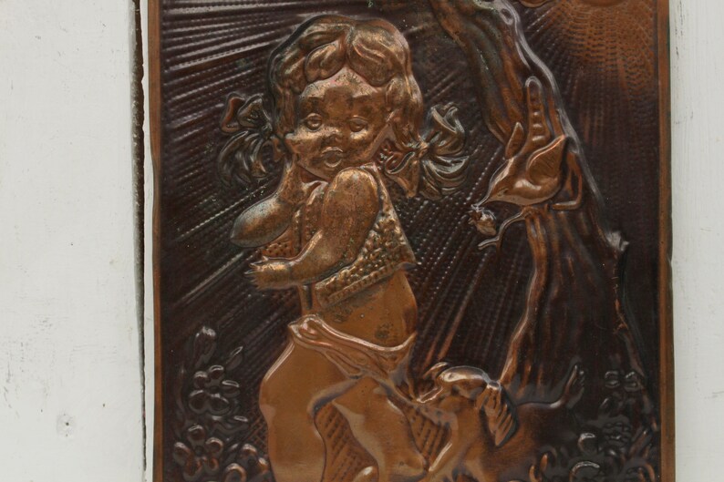 May include: A copper wall plaque with a raised relief design of a young girl with pigtails standing next to a tree. The girl is wearing a dress and holding a bird in her hand.