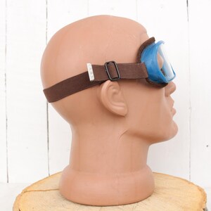 May include: Blue safety goggles with a brown adjustable strap. The goggles are on a mannequin head.