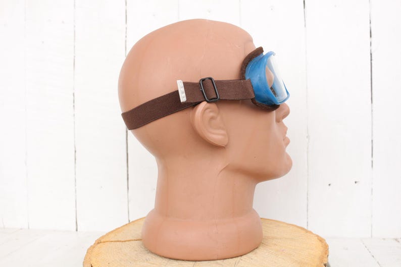 May include: Blue safety goggles with a brown adjustable strap. The goggles are on a mannequin head.