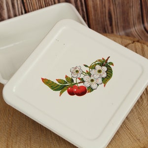 May include: A white enamel square dish with a matching lid. The lid features a colorful illustration of cherries, white blossoms, and green leaves. The dish is open, revealing the interior.