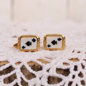 May include: A pair of gold cufflinks with a white background and black spades design.