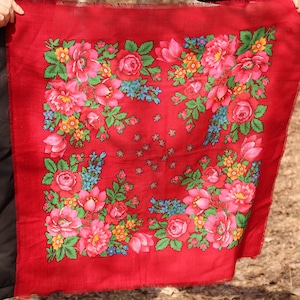 以下が含まれることがあります： 赤い生地のストールに花柄が描かれています。柄は、赤い背景にピンク、黄色、青、緑の花が描かれています。