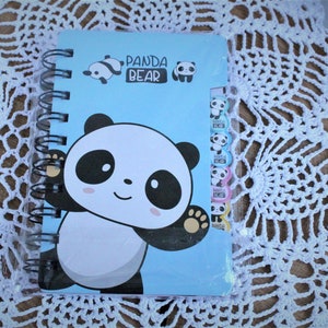K&ouml;nnte beinhalten: Ein blaues Spiralnotizbuch mit einem Pandab&auml;r-Design. Der Einband zeigt einen gro&szlig;en Pandab&auml;r mit schwarzen Augen und einem wei&szlig;en Gesicht. Der Text "Panda Bear" ist in schwarzen Buchstaben auf dem Einband gedruckt.