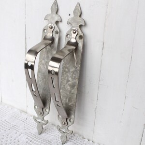 May include: Two silver metal door handles with ornate designs. The handles have a decorative, slightly textured finish.