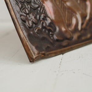 May include: A close-up of a brown and black ceramic tile with a raised design of a person riding a horse. The tile has a textured surface and a slightly curved edge.