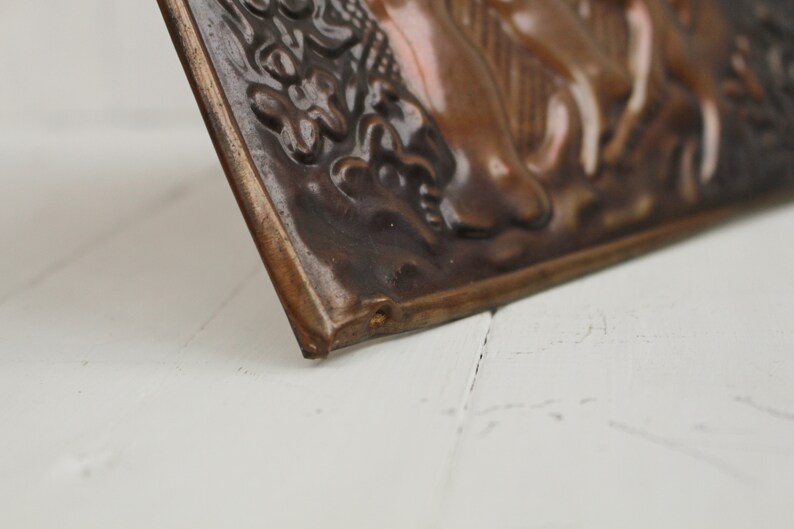 May include: A close-up of a brown and black ceramic tile with a raised design of a person riding a horse. The tile has a textured surface and a slightly curved edge.
