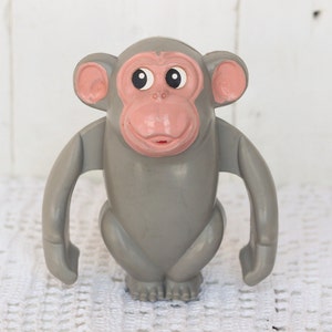 May include: A gray plastic toy monkey with pink ears and a pink face. The monkey has large black eyes and a wide smile.