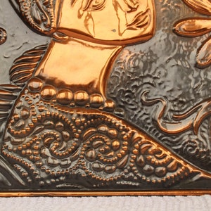 May include: A copper wall plaque with a raised design of a woman's face and a flower. The plaque has a dark brown patina and is embossed with intricate details.