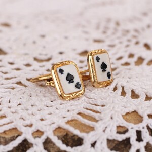 May include: A pair of gold cufflinks with a white enamel background and black spade suit design.