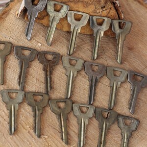 May include: A collection of 18 vintage keys, all made of metal and with a similar design. The keys are arranged in a semi-circle on a wooden surface.