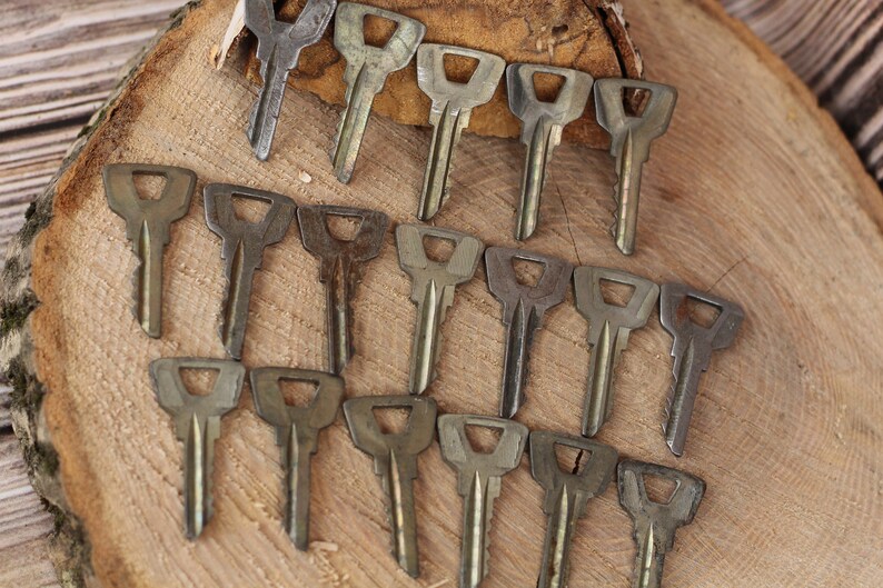 May include: A collection of 18 vintage keys, all made of metal and with a similar design. The keys are arranged in a semi-circle on a wooden surface.