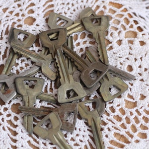 May include: A pile of old, tarnished keys with a square-shaped keyhole on a white crocheted doily.