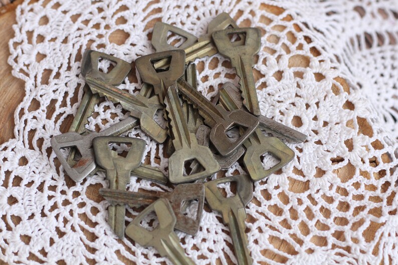 May include: A pile of old, tarnished keys with a square-shaped keyhole on a white crocheted doily.