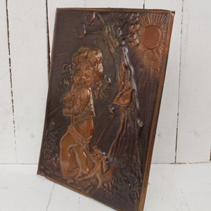 May include: A copper wall plaque with a raised relief design of a child holding a bird in a forest setting. The sun is shining brightly in the background.