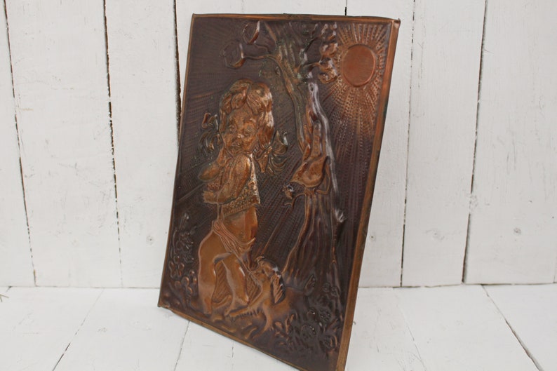 May include: A copper wall plaque with a raised relief design of a child holding a bird in a forest setting. The sun is shining brightly in the background.